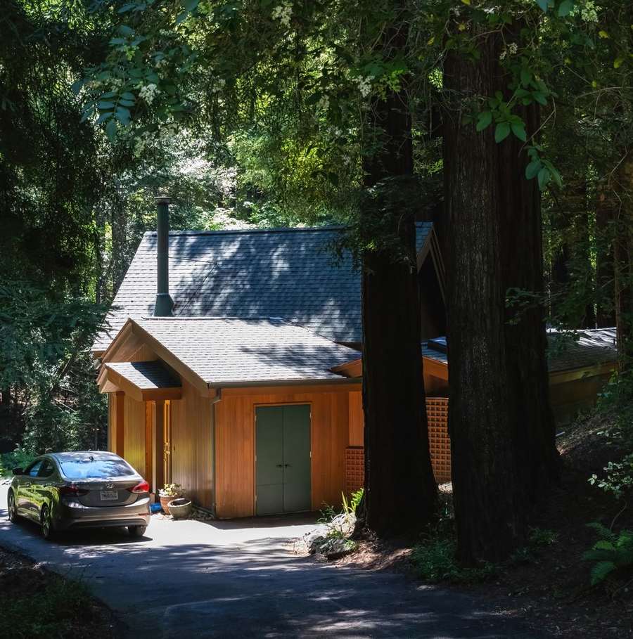 A wooden house in the trees with a car in the drive