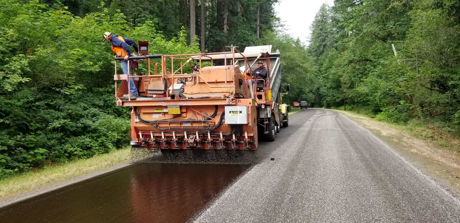 Stone chips being spread over hot liquid asphalt on a wooded road